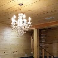 Crystal chandelier in a wood-paneled room with a staircase and warm ceiling lights.