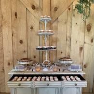 Tiered dessert display with trays of pastries on a wooden buffet table against a wood fence backdrop