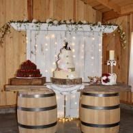 Rustic wedding dessert table with white cake, red cupcakes, barrels, and fairy lights