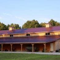Rustic two-story wooden building with a red roof at sunset, surrounded by trees and grass.