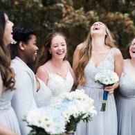 Bridesmaids in light dresses smiling and holding white bouquets outdoors at a wedding