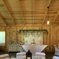 Rustic barn wedding reception with white-draped table, greenery backdrop, and lanterns