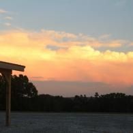 Sunset over smooth groomed field with orange clouds and a dark treeline silhouette
