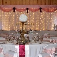Elegant banquet table with pink drapes, string lights, white linens, and gold centerpieces
