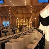 Decorated banquet hall with long tables, white chairs, and warm string lights in a rustic wooden room