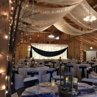 Elegant banquet hall with draped white fabric, chandeliers, and round tables set for an event