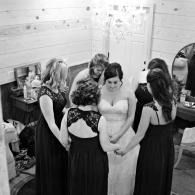 Five people in a room gather around a woman in a white dress, looking down at her hands.