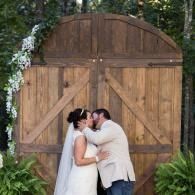 Bride and groom kissing in front of a wooden barn door at an outdoor wedding