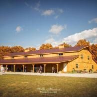 Sunlit yellow barn with porch and people on a grassy field under a blue sky