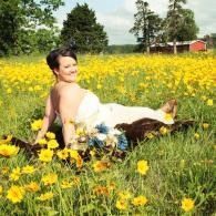 Person reclining in a sunny yellow flower field with trees and a red barn in the background