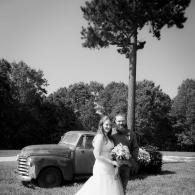 Bride and groom posing by a vintage pickup truck in a grassy field with trees