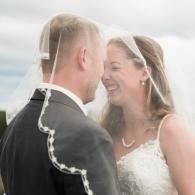 Bride and groom smiling closely under a veil outdoors