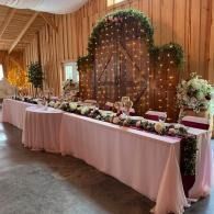 Decorated reception table with pink linens, floral arrangements, and fairy lights in a wood-paneled hall