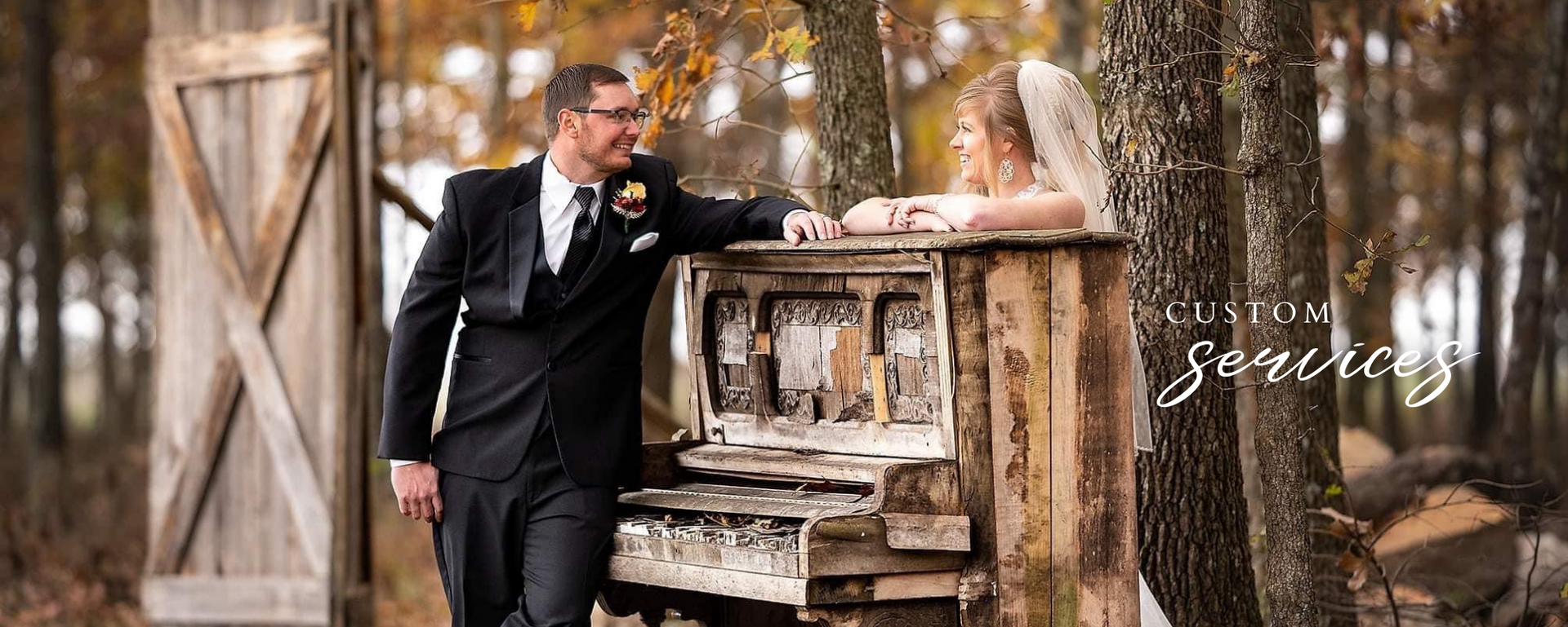 Man in a black suit leaning on an old piano in a rustic barn setting with soft brown tones