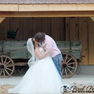 Bride and groom embracing in front of a wooden wagon and barn