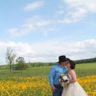 Couple kissing in wedding attire in a yellow wildflower field under a blue sky
