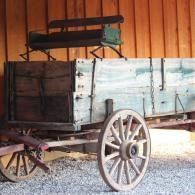 Old wooden horse-drawn wagon with large spoked wheels, parked in a barn-like shed.