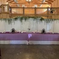 Purple-draped buffet tables in a rustic hall with wooden balcony and hanging greenery