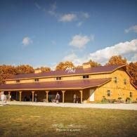 Yellow barn-style building with a porch under a blue sky, surrounded by autumn trees and grass