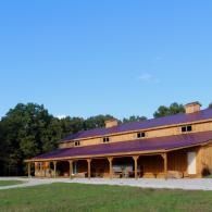 Single-story red-roofed building with wooden porch in a grassy field under a clear blue sky
