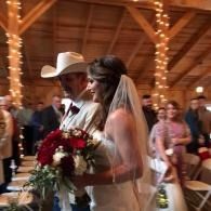 Bride and cowboy-hatted partner walking down the aisle in a rustic barn wedding