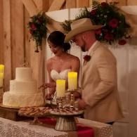 Bride and groom cutting a tiered wedding cake beside glowing candles at an indoor reception