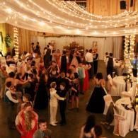 Crowded indoor dance floor under warm string lights, with guests mingling and dancing at a festive event