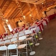 Elegant banquet hall with white chairs and red table settings under warm wooden beams