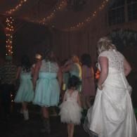 People in formal dresses walking through a dimly lit hall with string lights and draped decorations