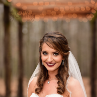 Bride in white dress and veil smiling at outdoor wedding ceremony with warm lights in background