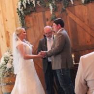 Wedding couple exchanging vows with officiant under floral arch indoors