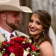 Bride and groom pose with a red bouquet; she smiles in a white dress and he wears a cowboy hat.