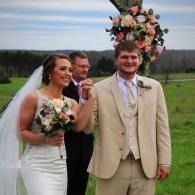 Bride and groom pose outdoors with a floral arrangement on a pole behind them
