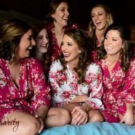 Group of women in pink floral robes, one in a reverse design white robe,  laughing together on a couch