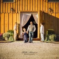 Four people stand at a barn doorway with white curtains, in warm evening light.