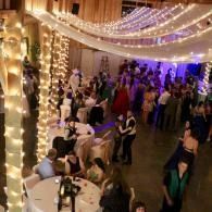 Crowded banquet hall with string lights, draped fabric, and guests mingling around tables and a dance floor