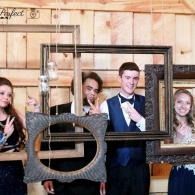 Four people posing behind empty picture frames at a rustic event venue.