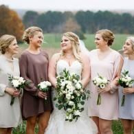 Bridal party standing outdoors, holding bouquets in soft pink and mauve dresses.