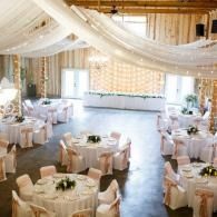 Decorated banquet hall with round tables, white chair covers, and draped fabric ceiling for a formal event