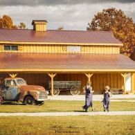 Two people walking past a rustic barn with a vintage truck under warm autumn light