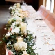 Long banquet table with white floral and greenery centerpieces and candle holders