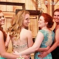 Four women in formal dresses standing close together at an indoor event, smiling and talking.