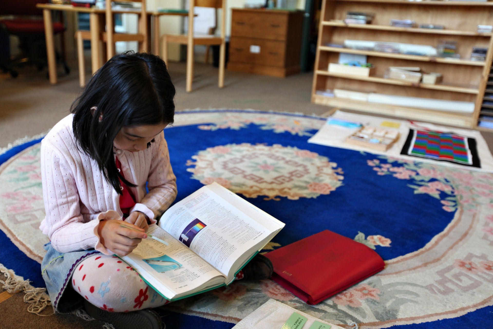 Child on the floor reading a book in a the Montessori classroom