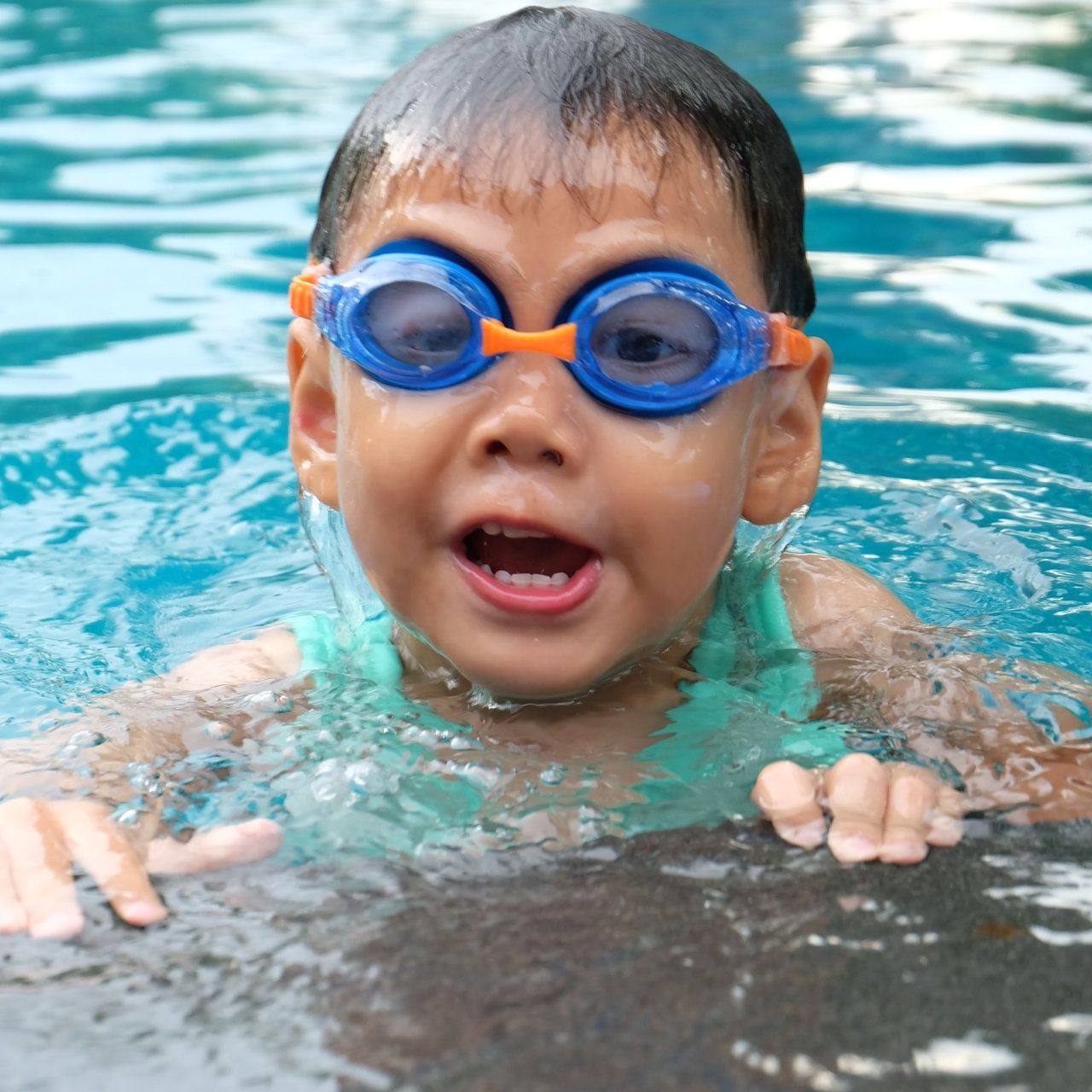 A young boy wearing goggles is swimming in a pool.