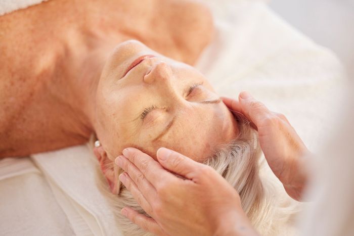 Person receiving facial massage; hands on forehead, eyes closed.