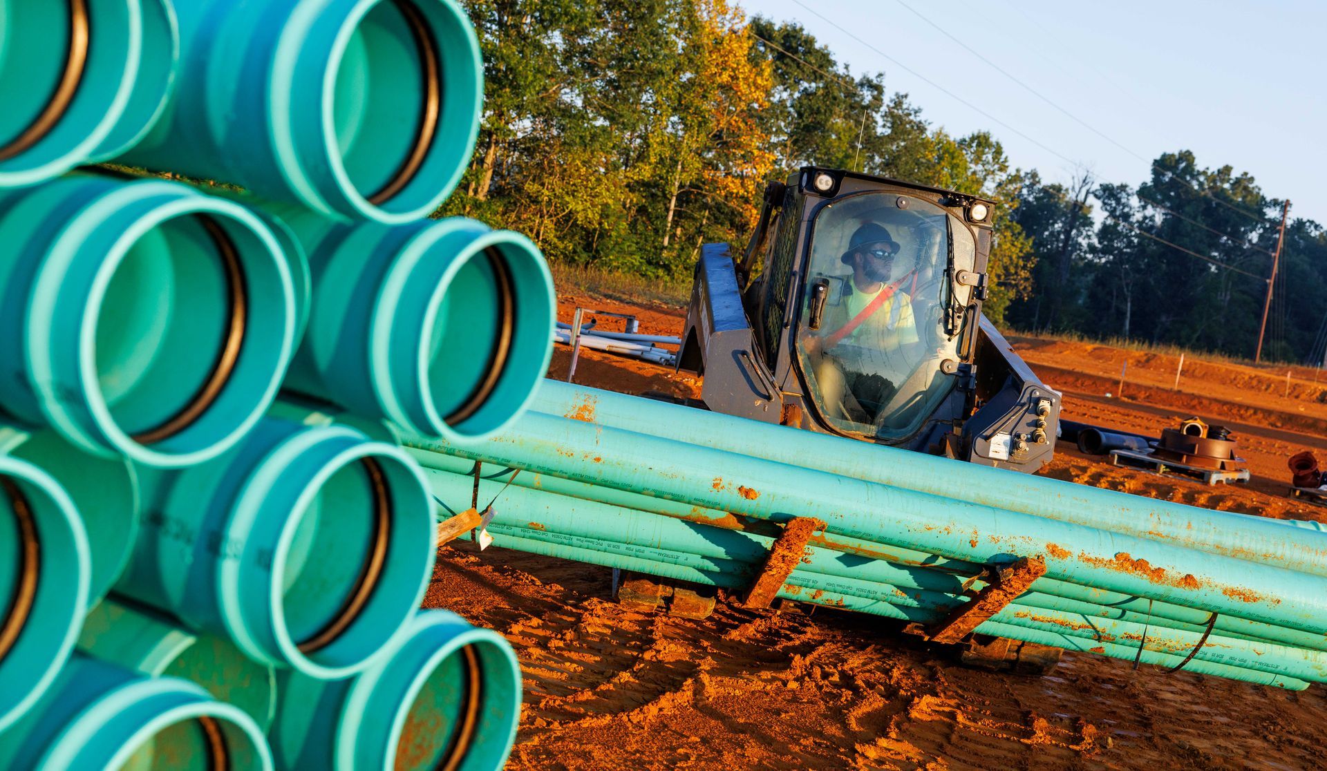 KZ Construction Team Member carrying piping with a large piece of construction machinery