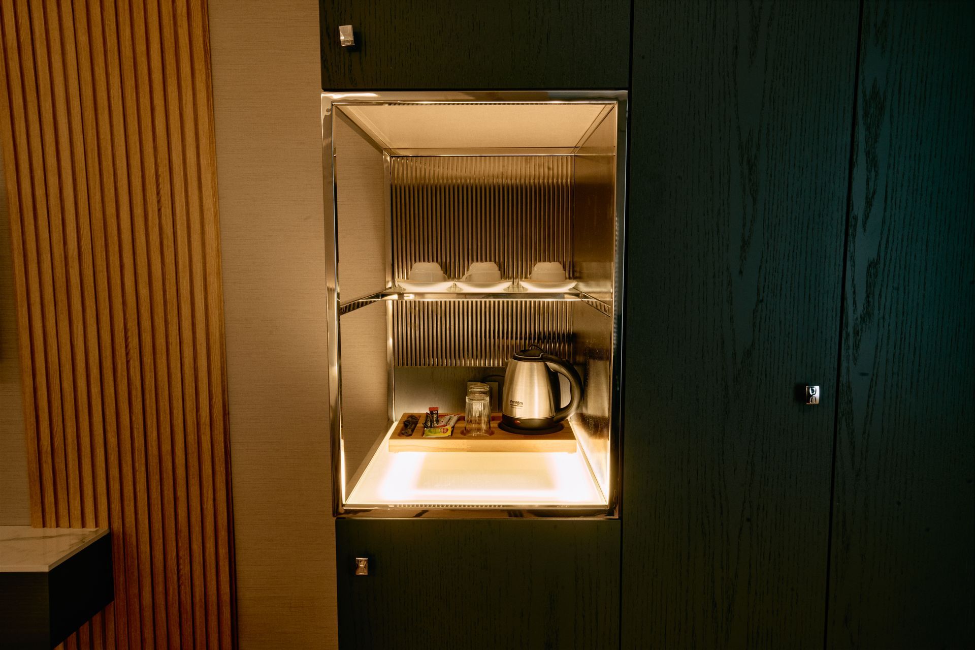 There is a shelf with a kettle and cups on it.