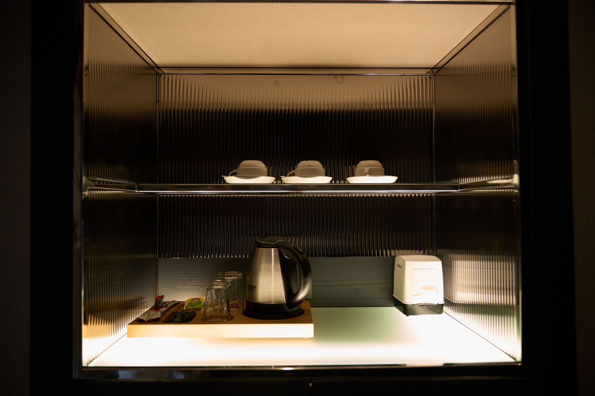 There is a shelf with a kettle and cups on it.