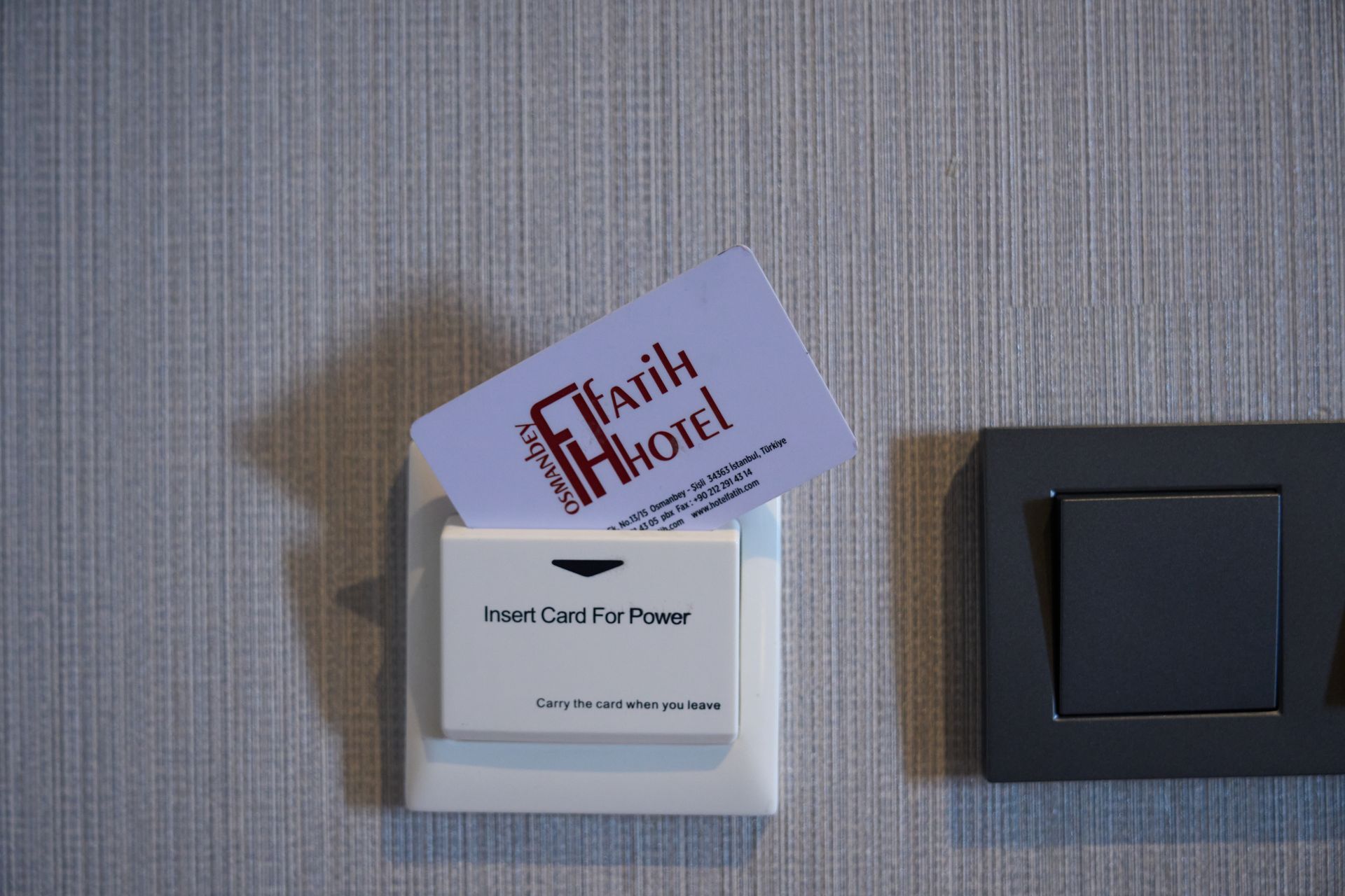 A hotel key card is sitting on a wall next to a light switch.