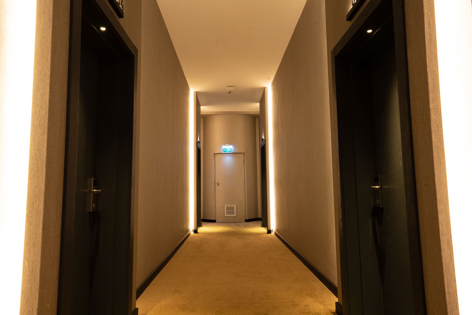A long hallway with a lot of doors and lights on the walls.
